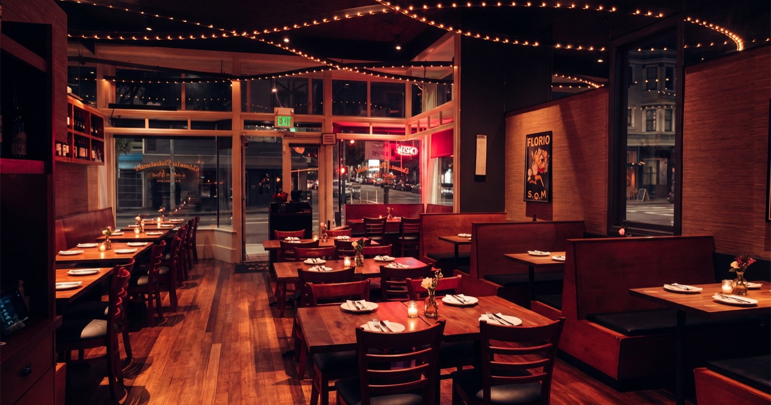 The corner dining room under string lights, windows onto the street at night